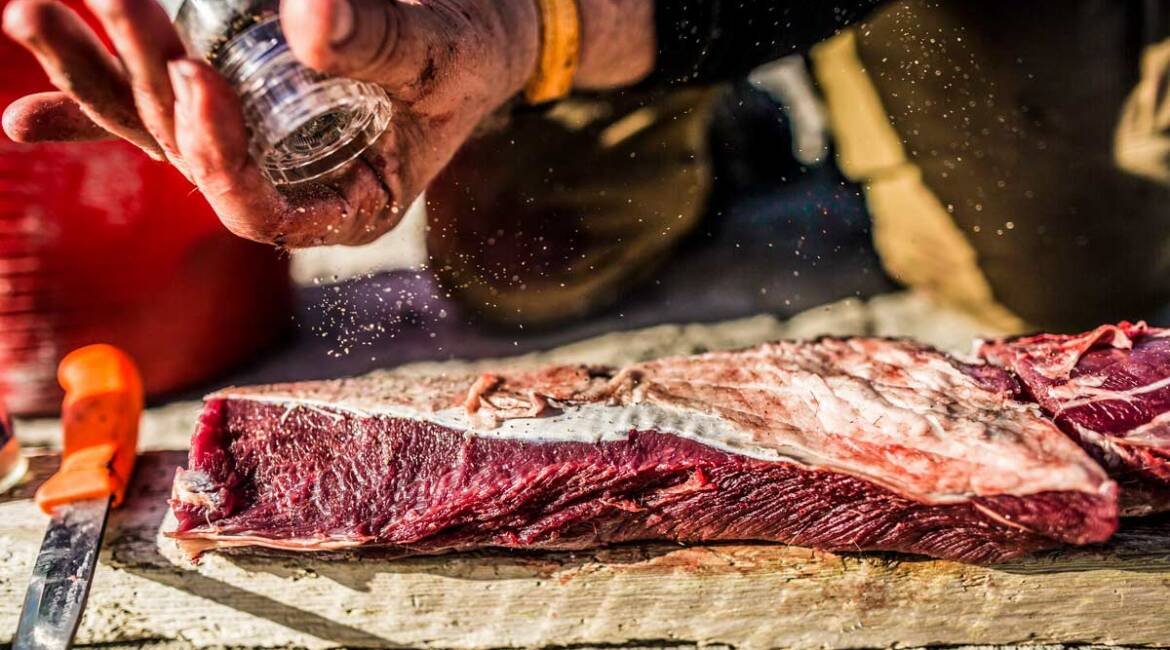 Un cazador echa pimienta sobre un trozo de carne de caza recién cobrada.