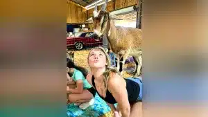 Una chica hace yoga con una cabra encima.