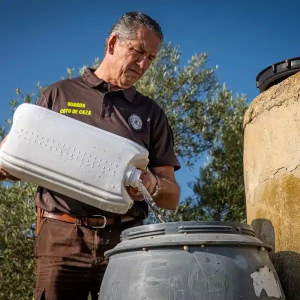 Un guarda de coto de caza rellena un bebedero.